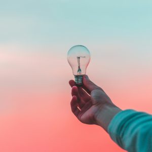 Person holding a lightbulb against a pink sky background